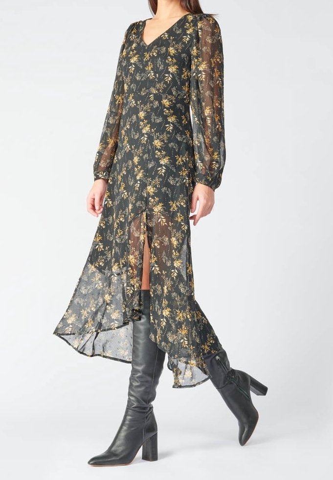 Femme portant une robe florale noire transparente à manches longues et des bottes noires à talons hauts montant jusqu'aux genoux, marchant avec un pied en avant.