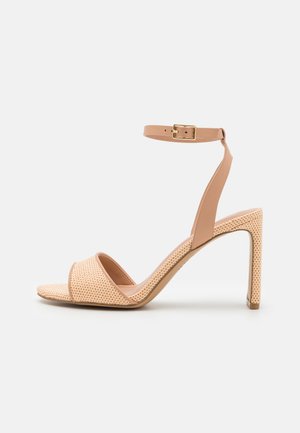 Beige högklackad sandal med perforerad rem och ankelspänne. Har en slank design, öppen tå och en texturerad yta.