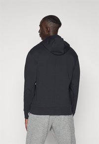 Črna kapuča s sweaterjem z gladko teksturo in rebrastimi manšetami. Preprost dizajn, pogled zadaj, v kombinaciji z sivimi trenirkami.