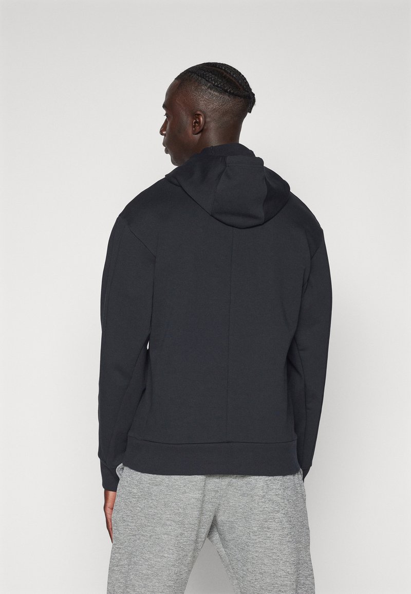 Felpa nera con cappuccio, dalla texture liscia e con polsini a coste. Design semplice, vista posteriore, abbinata a pantaloni sportivi grigi.