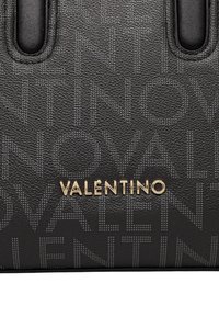 Pelle nera testurizzata con motivo in rilievo del testo Valentino e logo Valentino in metallo dorato su una borsa.