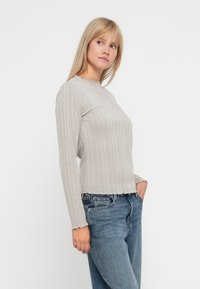 Lichtbeige geribde langemouwen top met een gegolfde halslijn en zoom, gecombineerd met blauwe jeans, met een ontspannen pasvorm en een zachte textuur.