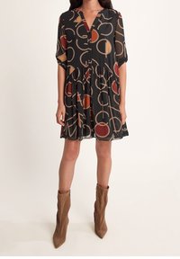 Svart klänning med korta ärmar, V-ringning och åtsittande midja; har abstrakta mönster i rött och orange, med en fladdrande fåll. Bruna ankelstövlar.