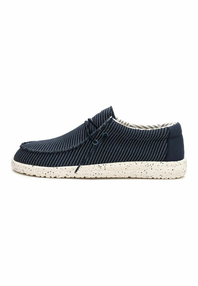 Zapatos casuales azul marino con parte superior de tela texturizada, que cuentan con suelas moteadas en blanco y un diseño con cordones. El interior tiene un patrón a rayas.