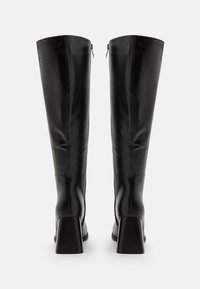 Knee-high black leather boots with a glossy finish, square heels, and rear zipper closures, featuring seam detailing along the shafts.
