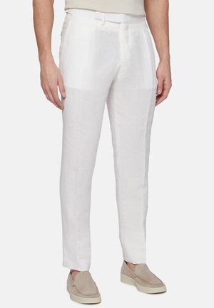 Pantalons en lin blanc avec une coupe droite, devant plat et poches latérales, associés à des chaussures à enfiler beiges. Tissu léger et respirant.