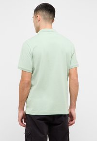 Šviesiai žalias polo marškinėlis, pagamintas iš medvilnės, su klasikine apykakle ir trumpomis rankovėmis, tiesiu sijonu ir subtilia tekstūra.
