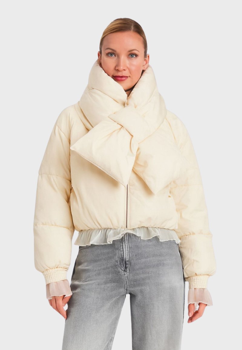 Giacca imbottita color crema con ampio colletto a fiocco, design corto, orlo arricciato e polsini trasparenti, abbinata a jeans grigio chiaro.