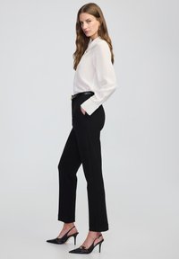 Bílé halenka s dlouhými rukávy, černé kalhoty na míru a černé lodičky na vysokém podpatku. Má elegantní design a texturovanou látku.