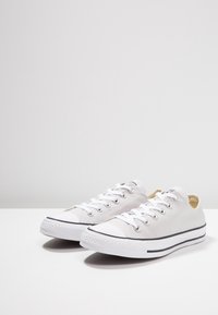 Baskets basses blanches en toile avec bout rond, accents noirs, œillets argentés, et semelles en caoutchouc blanc. Design classique à coupe basse avec tissu texturé.