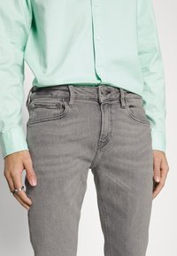 Jeans de mezclilla gris con un ajuste clásico, que cuentan con bolsillos delanteros y un cierre de botones, complementados con una camisa de botones en verde menta.
