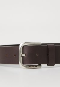 Bruine leren riem met een zilveren metalen gesp. Beschikt over vijf gaatjes voor maataanpassing en is gegraveerd met 'REPLAY' op de gesp.