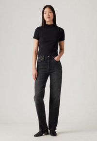 Μαύρο εφαρμοστό t-shirt σε συνδυασμό με ψηλόμεσο, ίσιο παντελόνι τζιν σε σκούρο γκρι. Το σύνολο χαρακτηρίζεται από ελάχιστα μεταλλικά στοιχεία και ομαλή υφή.