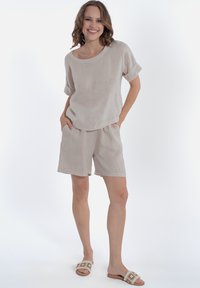 Top di lino beige chiaro con maniche corte arrotolate e vestibilità morbida, abbinato a pantaloni corti in lino coordinati. L'outfit presenta un design casual e tasche.