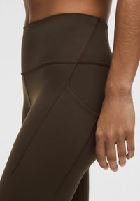 Suure lähedalt vaade inimesest, kes kannab tumesiniseid kõrge vöökohtadega retuuse, millel on nähtavad õmblused ja küljetasku, käsi lõdvestatult reie kõrval.