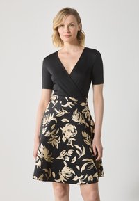 Robe noire avec un haut ajusté à col en V et manches courtes, se prolongeant en une jupe évasée ornée de motifs floraux dorés.