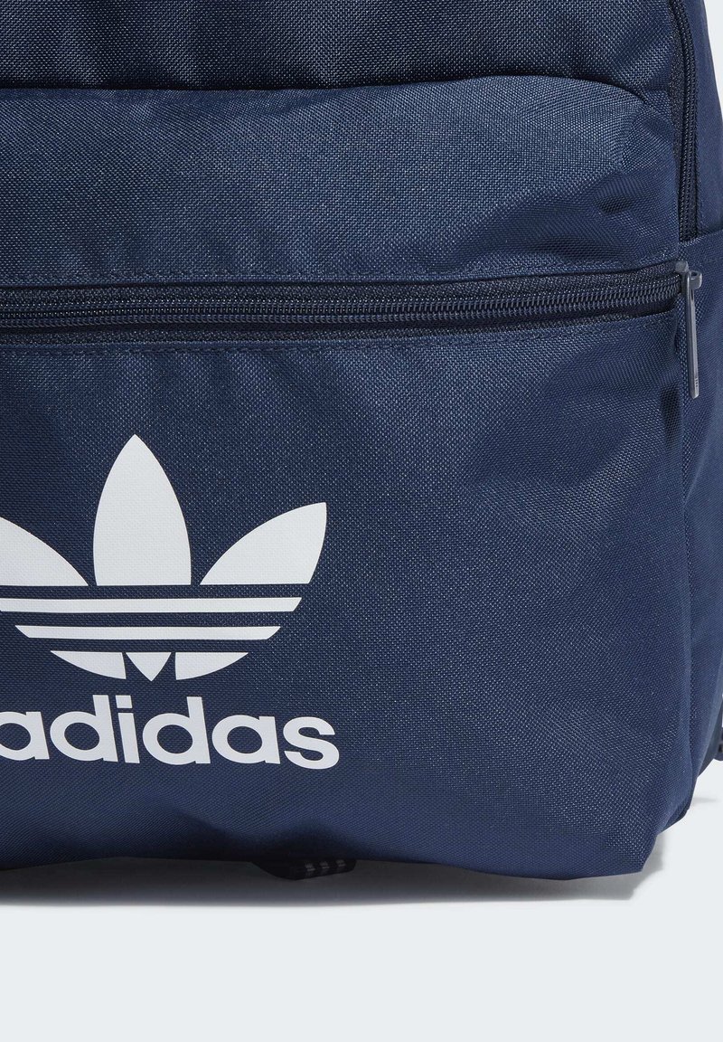 Zaino blu navy con logo Adidas bianco e tre strisce, realizzato in tessuto texture con tasca anteriore con zip.