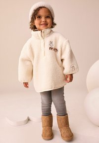 Kreemivärvi fliispullover kõrge krae, ette nööpide ja "miffy" tikandiga. Koos hallide retuuside ja pruunide saapadega, millel on jänesemuster.