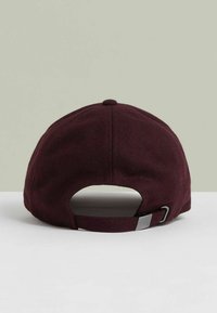 Burgundowa regulowana czapka baseballowa pokazana z tyłu, z metalowym zapięciem i materiałowym paskiem na białej powierzchni i jasnoszarym tle.