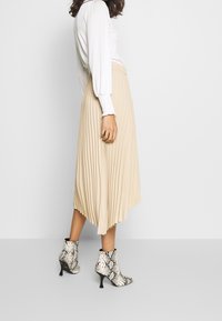 Falda plisada beige con cintura elástica, combinada con botines de tobillo de estampado de serpiente en blanco y negro, que exhiben un diseño texturizado.