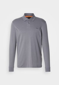 Sivi dugi rukav polo majica od pamuka s tri gumba na izrezu. Sadrži suptilan logo na lijevoj strani prsnog koša. Glatka tekstura.