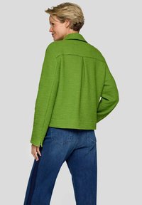 Grüne, strukturierte Jacke mit Kragen, mit einem kastigen Design und einer Rückenfalte, kombiniert mit blauen Denim-Jeans.