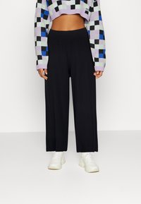 Černé kalhoty s širokými nohavicemi z texturované tkaniny, spárované s cropped svetrem s vícebarevným kostkovaným vzorem. Celkový look doplňují bílé tenisky.