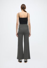 Musta hihaton toppi ja korkeavyötäröiset, leveälahkeiset harmaat ribbineulospöksyt. Sileä pinta pystysuorilla viivoilla. Rento jalkineet viimeistelevät asun.