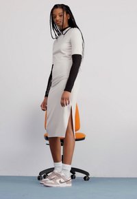 Lys grå tettsittende kjole med korte ermer og sideslipp. Lagd over en svart langermet topp. Kombinert med hvite sokker og beige joggesko.