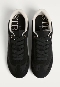 Baskets de sport noires avec une tige en suède et en tissu, dotées de lacets ronds, d'un col rembourré et d'un logo discret sur la semelle intérieure.