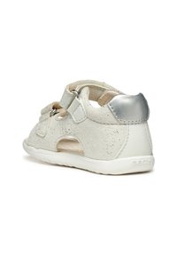 Białe skórzane sandały z teksturowanym wierzchem, zapięciem na rzep, wyciętymi bokami i srebrnym akcentem na obcasie. Posiadają amortyzowaną podeszwę dla komfortu.