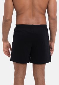 Zwarte katoenen shorts met een elastische tailleband, met een rechte snit en een gladde textuur, gezien vanaf de achterkant op een blote torso.