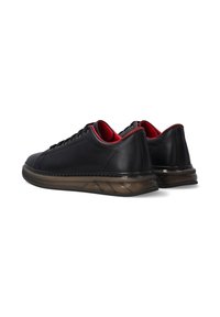 Schwarze Ledersneaker mit roten Akzenten, abgerundeter Form und durchsichtiger Gummisohle mit detaillierten seitlichen Rillen.