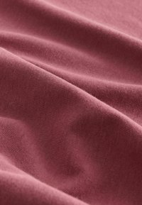 Textiel in zachte, roze stof met een subtiele textuur. Het materiaal lijkt licht gekreukeld en toont een glad, egaal oppervlak.