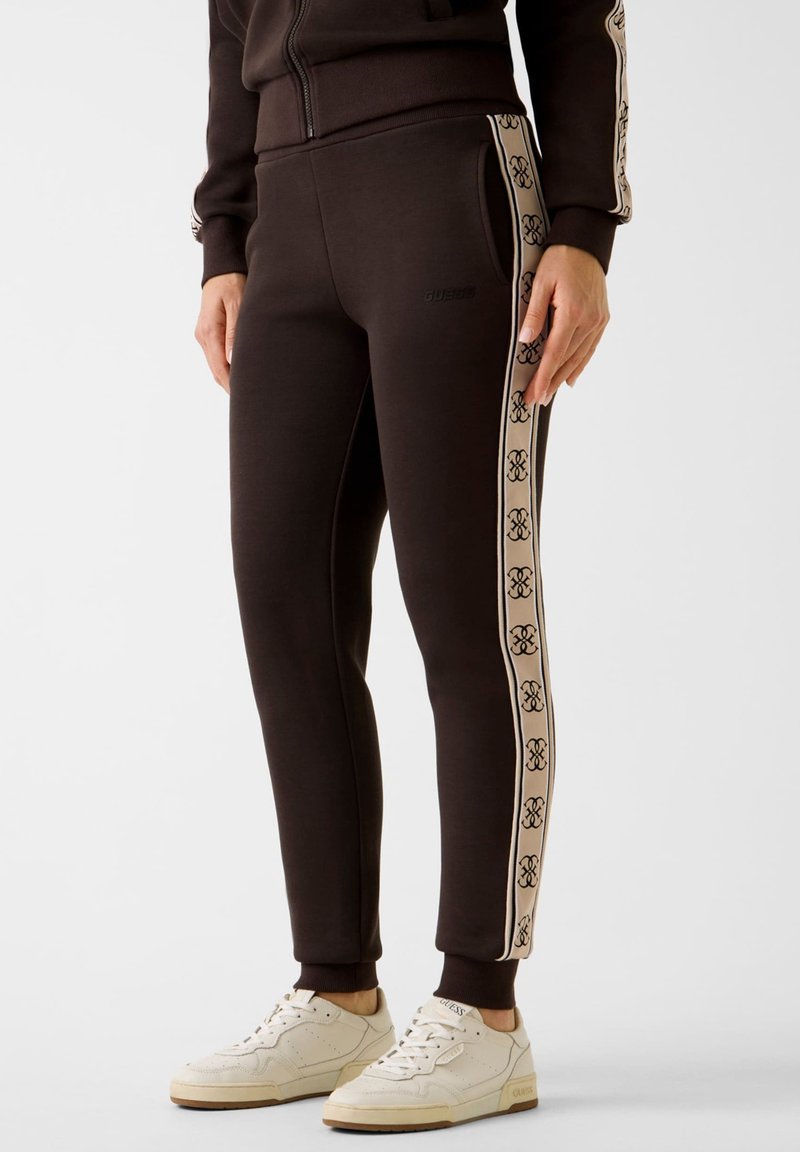 Czarne dopasowane spodnie dresowe z beżowym paskiem z logo po bokach, z kieszeniami z przodu, w połączeniu z białymi sneakersami na gumowej podeszwie.