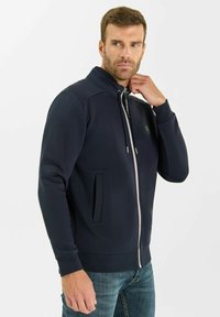 Giacca zip-up blu navy con colletto rialzato, tasche frontali e zip a contrasto. Realizzata in un tessuto testurizzato. Design slim fit.