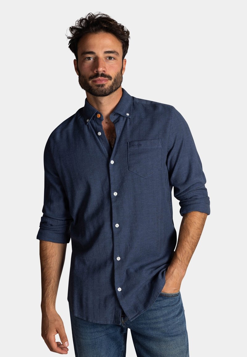 Donkerblauw button-up shirt voor mannen, met lange mouwen opgerold bij de manchetten, een borstzak en witte knopen. De stof heeft een gestructureerde uitstraling.