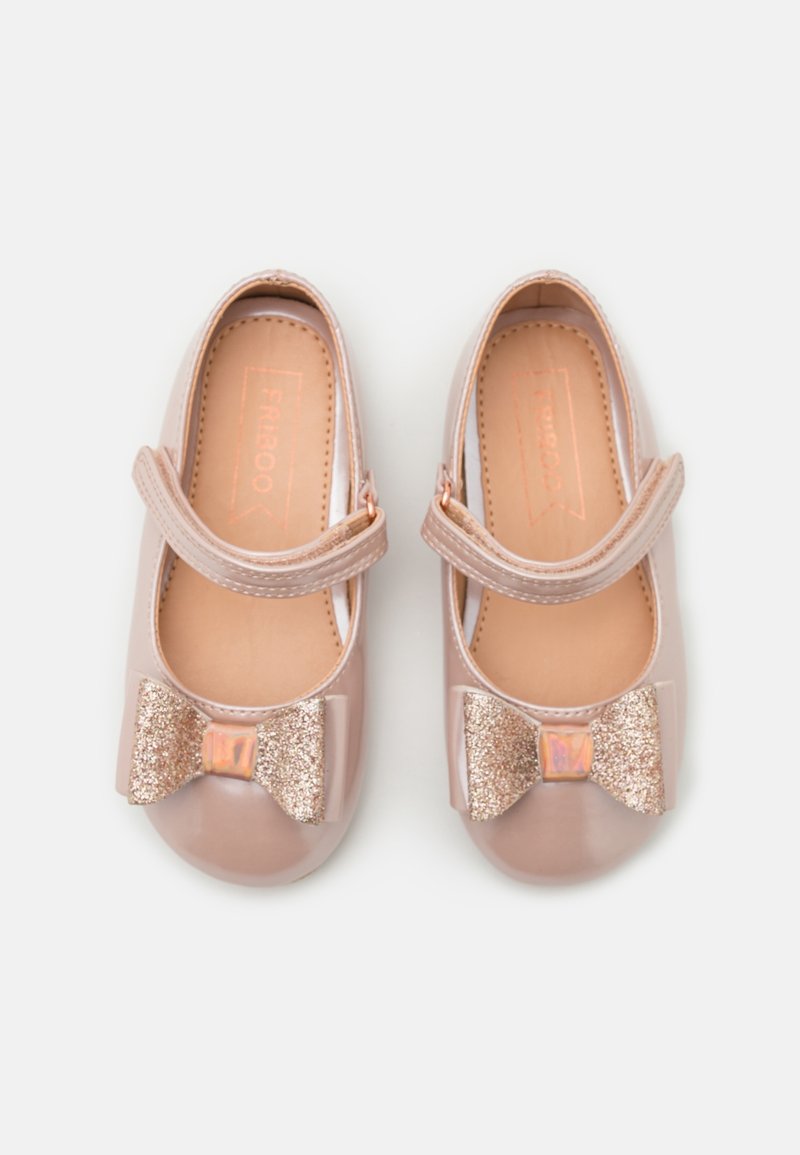 Paire de chaussures beige brillantes pour tout-petits avec nœuds pailletés et brides ajustables sur un fond blanc uni.