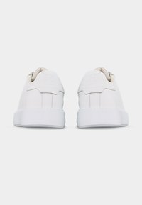 Ζευγάρι λευκών αθλητικών παπουτσιών χαμηλού τύπου, που φαίνονται από πίσω, με καθαρές ραφές και απλές παχιές σόλες σε λευκό φόντο.