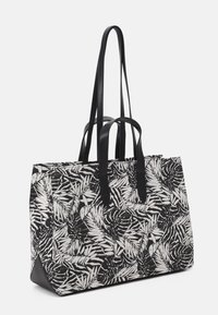 Kabelka vyrobená z černobílé tkaniny s motivem listů, se dvěma dlouhými koženými popruhy a vyztuženými uchy pro zvýšení odolnosti.