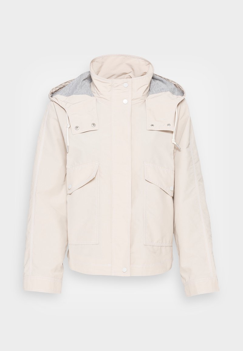 Chaqueta beige clara con un alto cuello, forro gris, dos bolsillos en el pecho y cierres a presión. El material parece suave con detalles de costura visibles.
