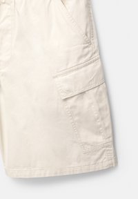 Beżowe szorty cargo wykonane z bawełny, z bocznymi kieszeniami i przeszyciami. Tkanina ma gładką, matową fakturę.