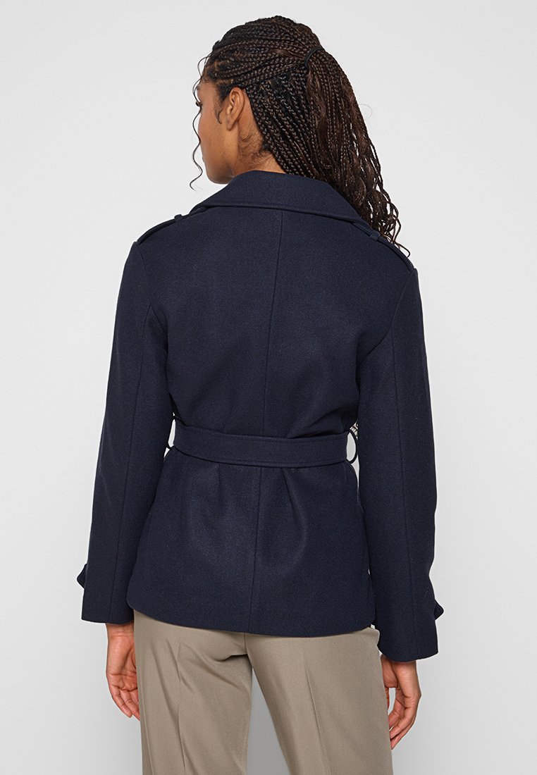 Manteau en laine mélangée bleu marine avec une taille ceinturée, de larges revers et des épaules structurées. Il présente des manches longues et une coupe ajustée à l'arrière.
