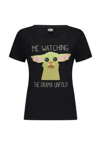 Black cotton t-shirt with short sleeves, round neckline, featuring a cartoon character with green skin and pink ears, and text that reads "ME WATCHING THE DRAMA UNFOLD."
