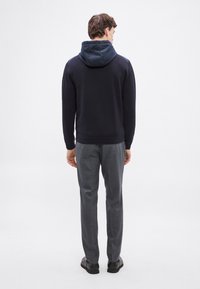 Jūras flotes džemperis ar kontrastējošu kapuci, kombinēts ar pelēkām piegrieztām biksēm. Mīksta tekstūra, piegulošs dizains un redzamas šūšanas detaļas.