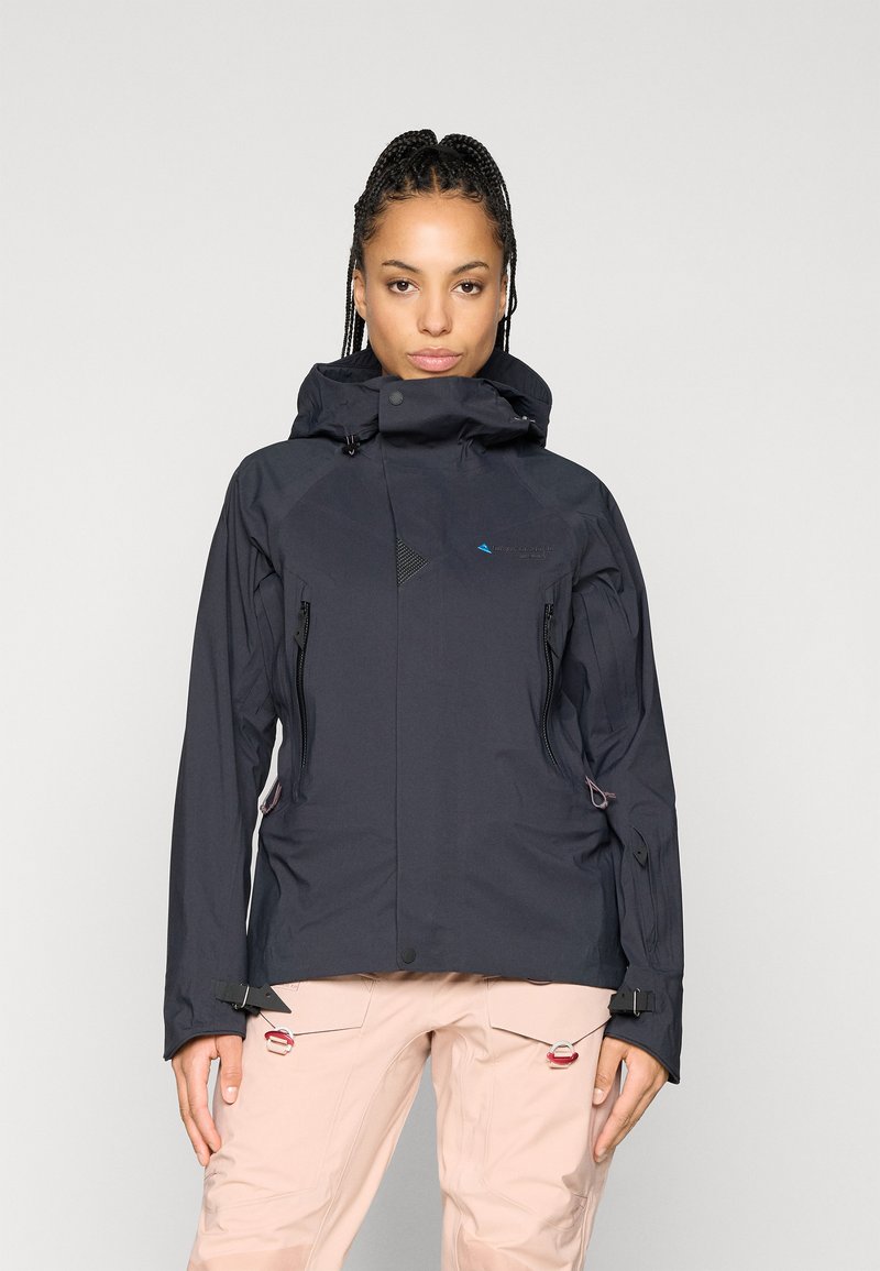 Crna vodootporna jakna s visokim ovratnikom, podesivom kapuljačom, zatvorenim džepovima i teksturiranim detaljima. Karakterizira je elegantan, moderan dizajn.