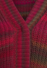 Stickad tröja med V-ringning, texturerad mönster och en gradient av röd, rosa och brun nyanser med ribbade kanter.