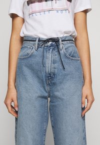 Světle modré denimové kalhoty s volným střihem a vysokým pasem, se černým šňůrkovým páskem a prošitím na kapsách. Tričko s grafickým potiskem.