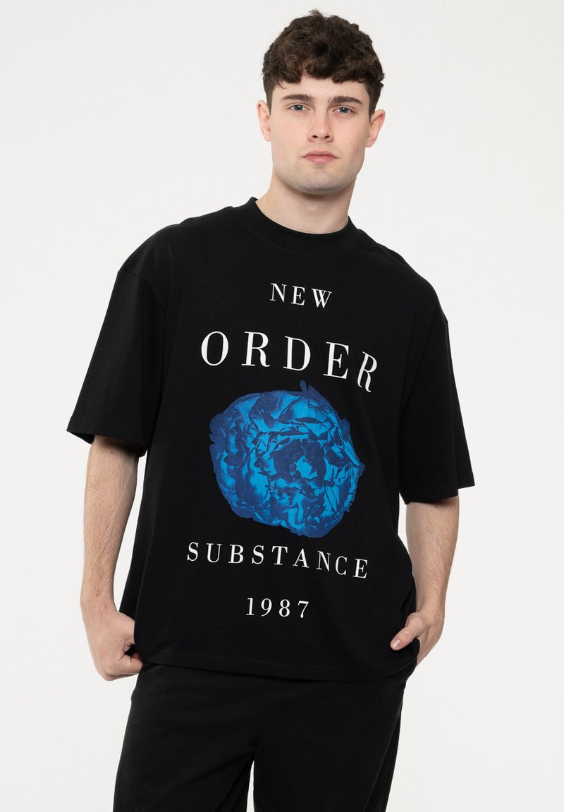Black oversized t-shirt featuring a blue graphic design of a circular shape with the text "NEW ORDER SUBSTANCE 1987" in white.