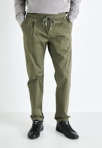 Pantalones livianos de color verde oliva con cintura elástica, cordón ajustable y bolsillos laterales; combinados con zapatillas negras.